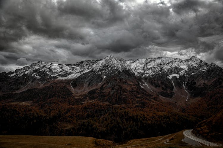 Landscape Of Rocky Snowcapped Mountains Under A Dramatic Cloudy Sky 