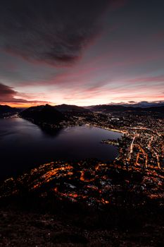 Captivating aerial cityscape of Lugano, Switzerland with a vibrant sunset overlooking the lake.