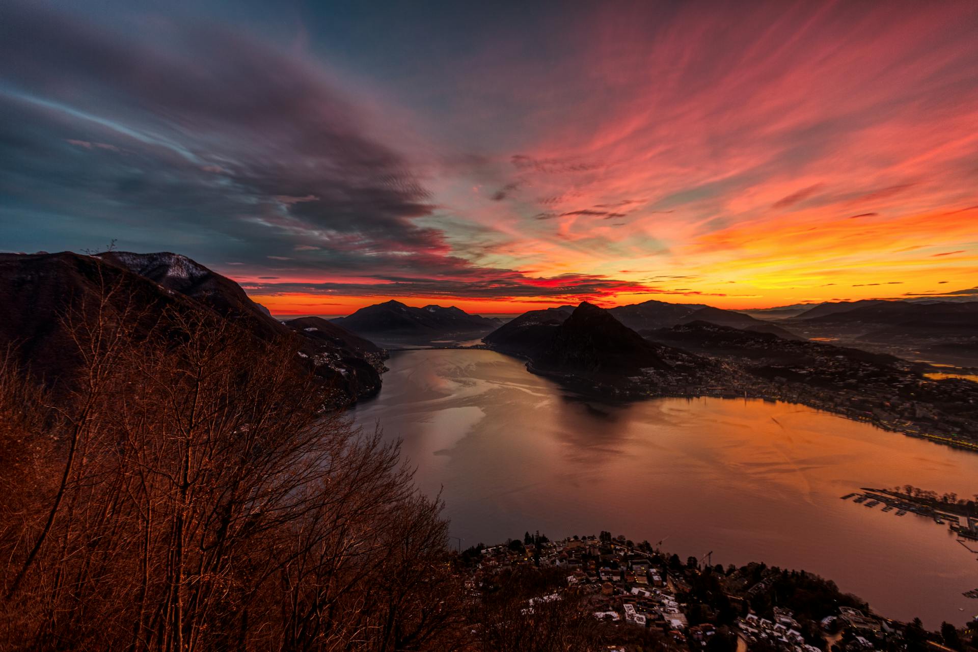 A breathtaking aerial view of Lake Lugano during a vibrant sunset from Brè sopra Lugano, Switzerland.