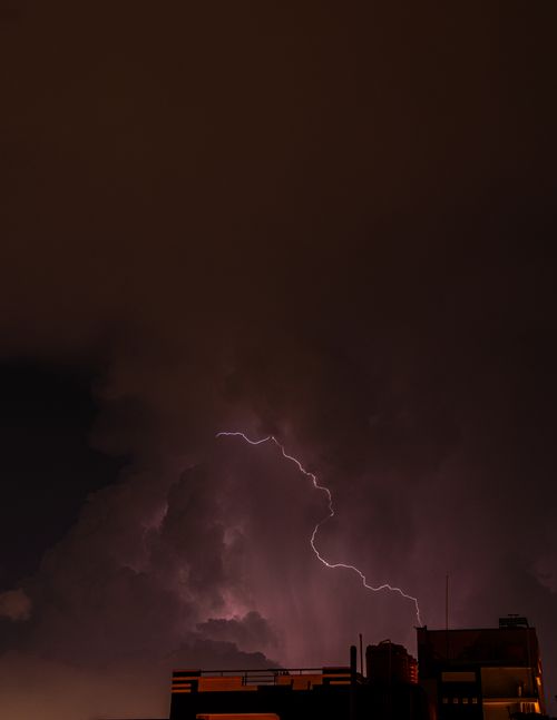 Free Striking lightning in a stormy night sky illuminates a cityscape's silhouette, capturing nature's raw power. Stock Photo