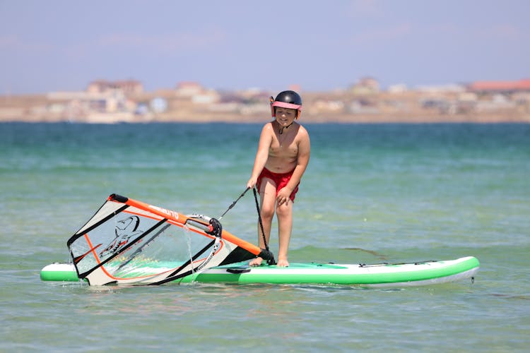 Boy In Helmet Standing On Board Surfing