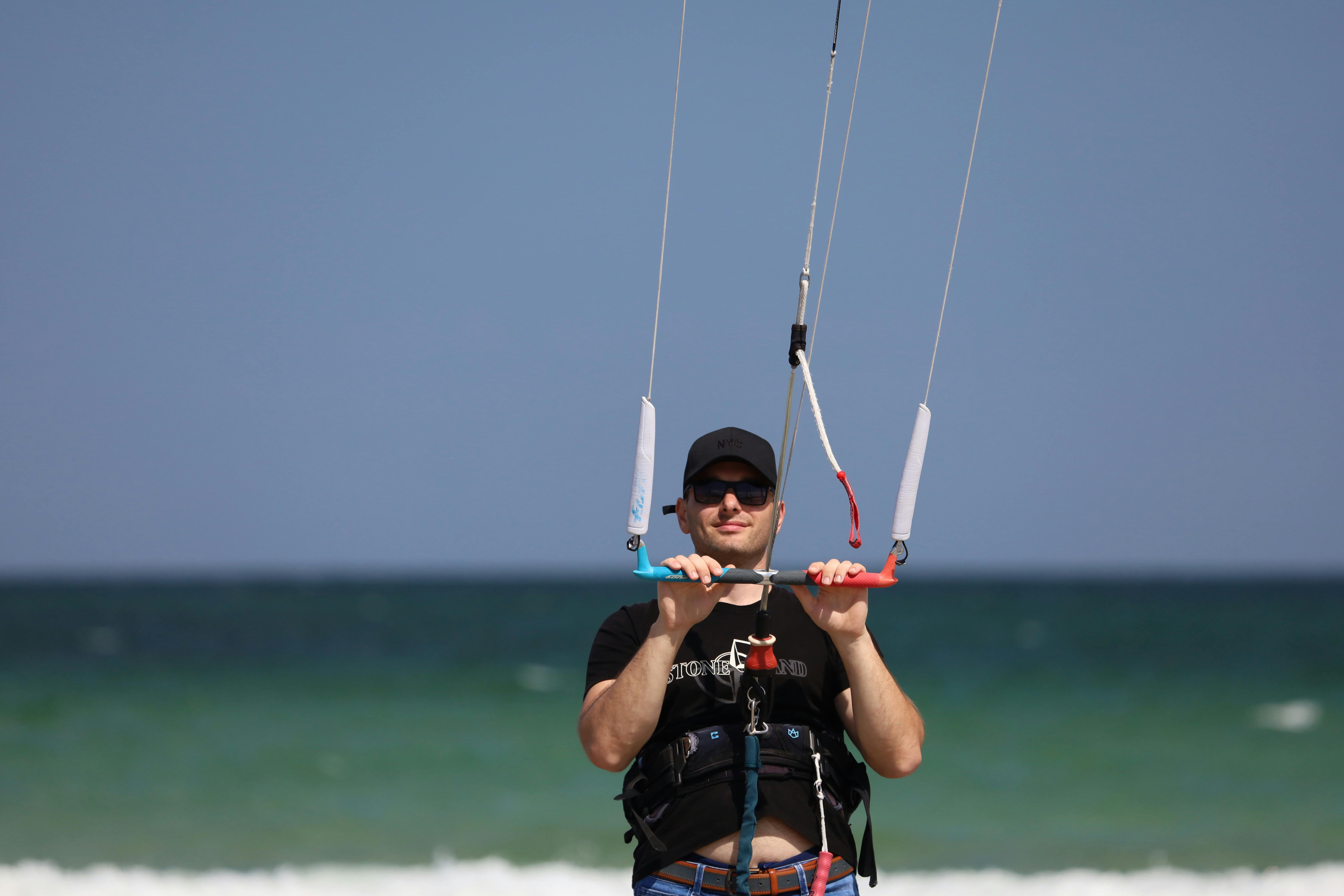 Man in Black Shirt with Black Cap Holding On to a Kitesurfing Control