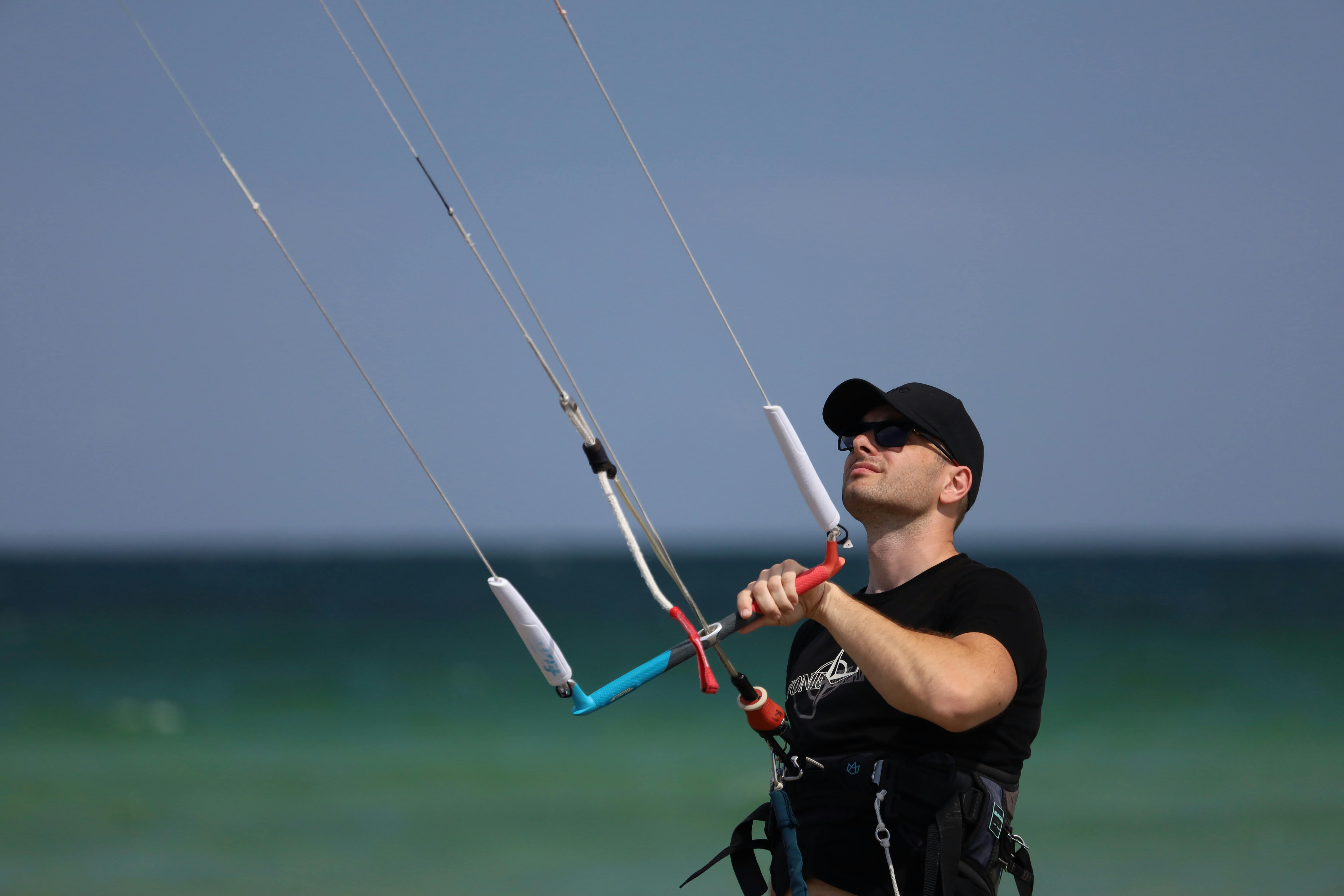 Man in Black Shirt and Black Cap Holding On to a Kitesurfing Control