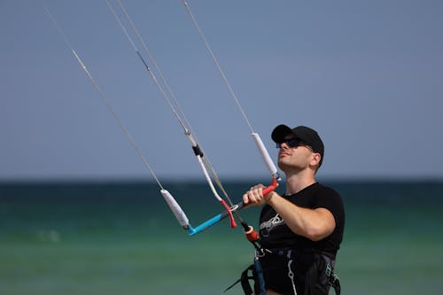 Man in Black Shirt and Black Cap Holding On to a Kitesurfing Control Bar 