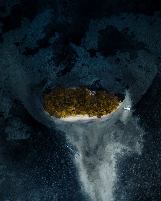 A breathtaking drone shot of an isolated island in the Philippine archipelago surrounded by deep blue ocean.