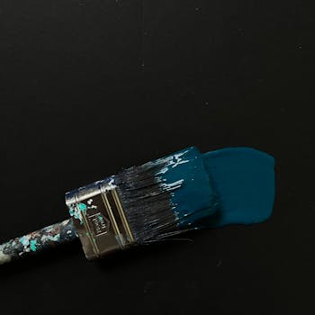 A close-up image of a paintbrush laying down a stroke of blue paint on a dark background.