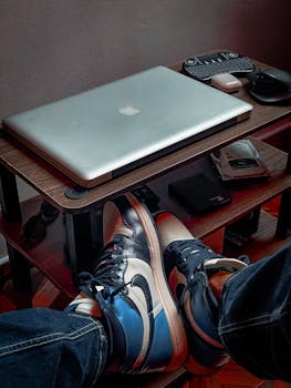 A stylish workspace setup featuring a laptop, sneakers, and tech gadgets on a wooden rack.