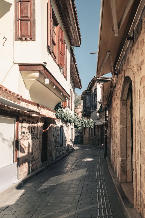 Free Quaint sunlit alley with rustic architecture in a historic European town, ideal for travel themes. Stock Photo