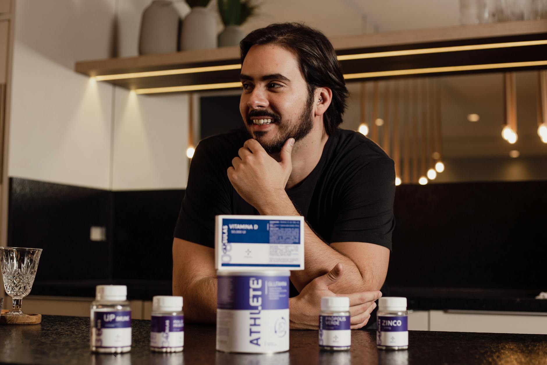 A man enjoying wellbeing surrounded by supplement bottles in a modern kitchen.