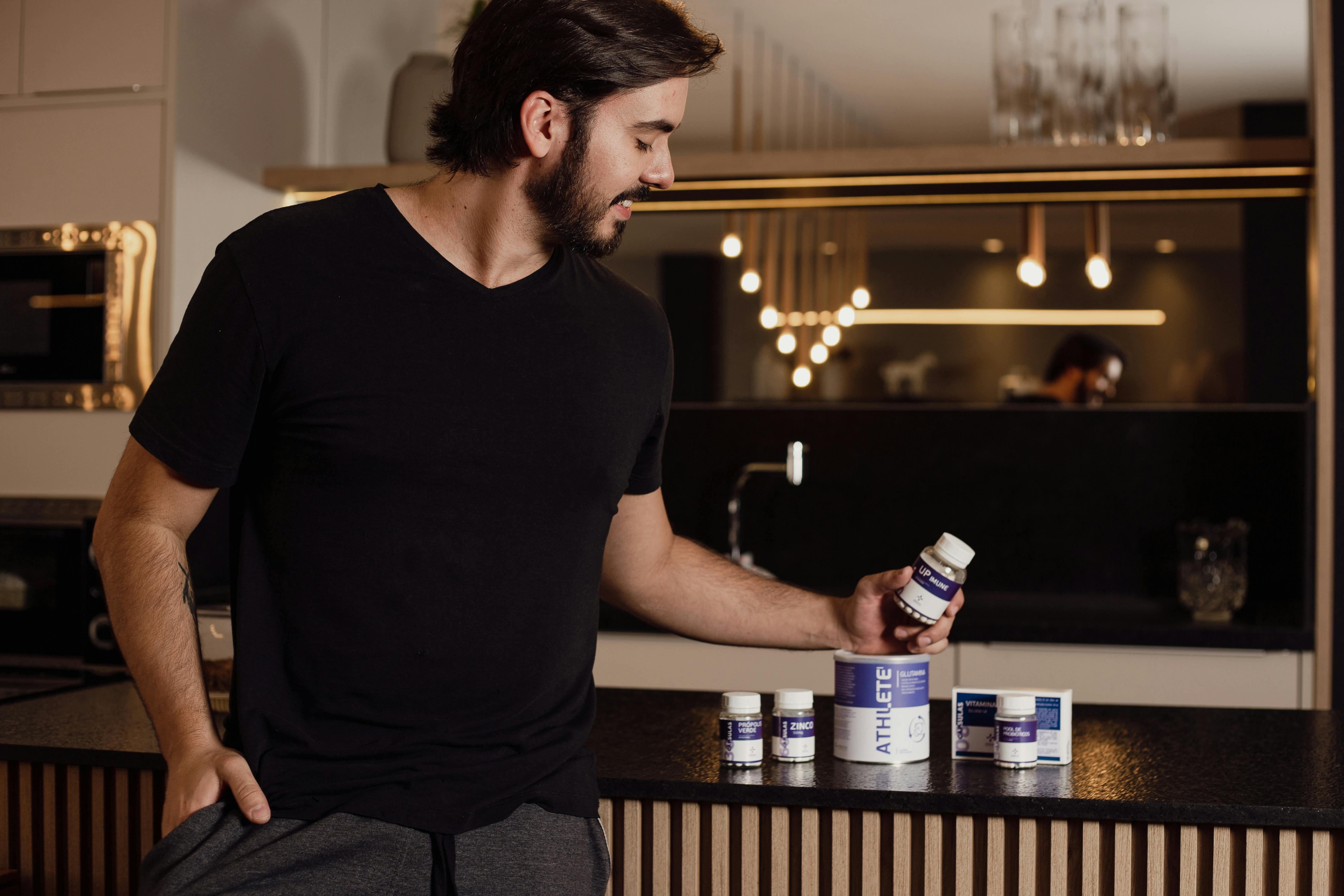 a man in black shirt looking at the bottle of supplement he is holding