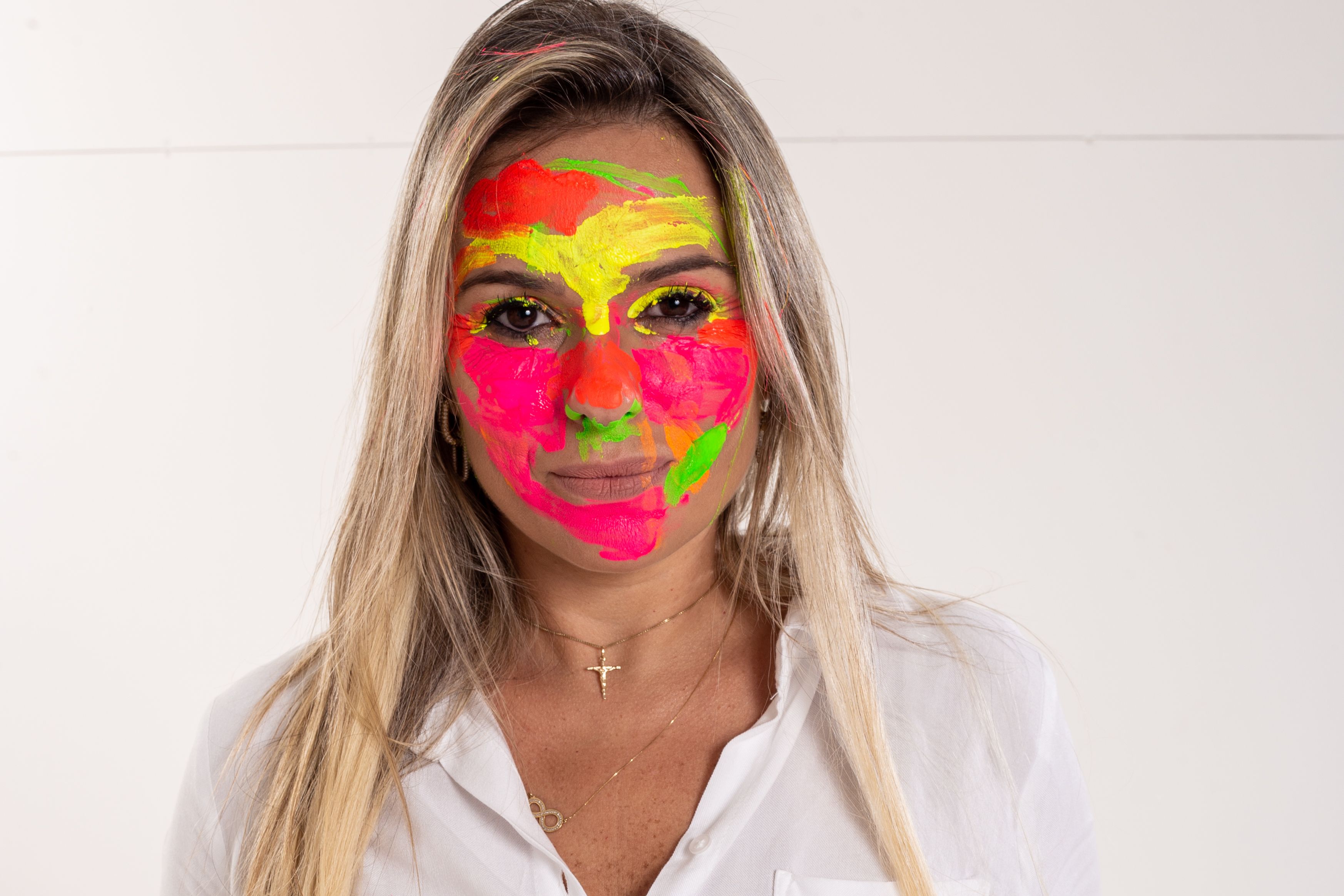 Colorful face paint art on woman's portrait, featuring bold neon hues in a studio setting.