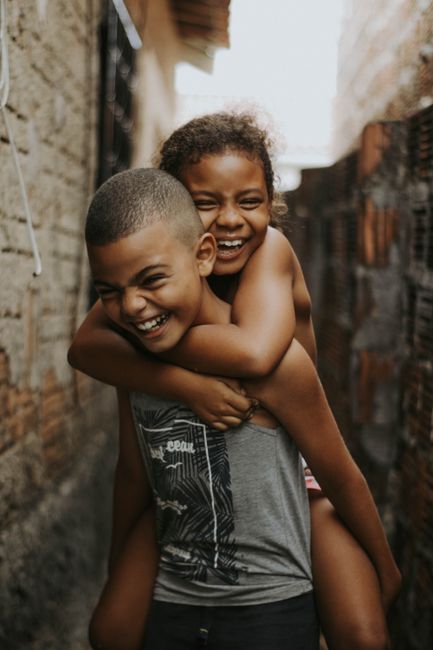 Two children laughing and playing piggyback in a narrow alley, enjoying a cheerful outdoor moment.