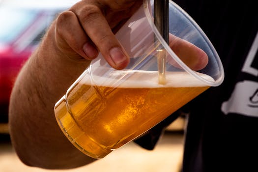 Close-up of a person pouring golden craft beer into a clear plastic cup.