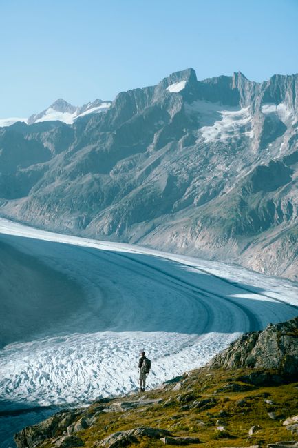 A lone hiker gazes at the stunning panoramic view of the Alps and Aletsch Glacier in Switzerland.