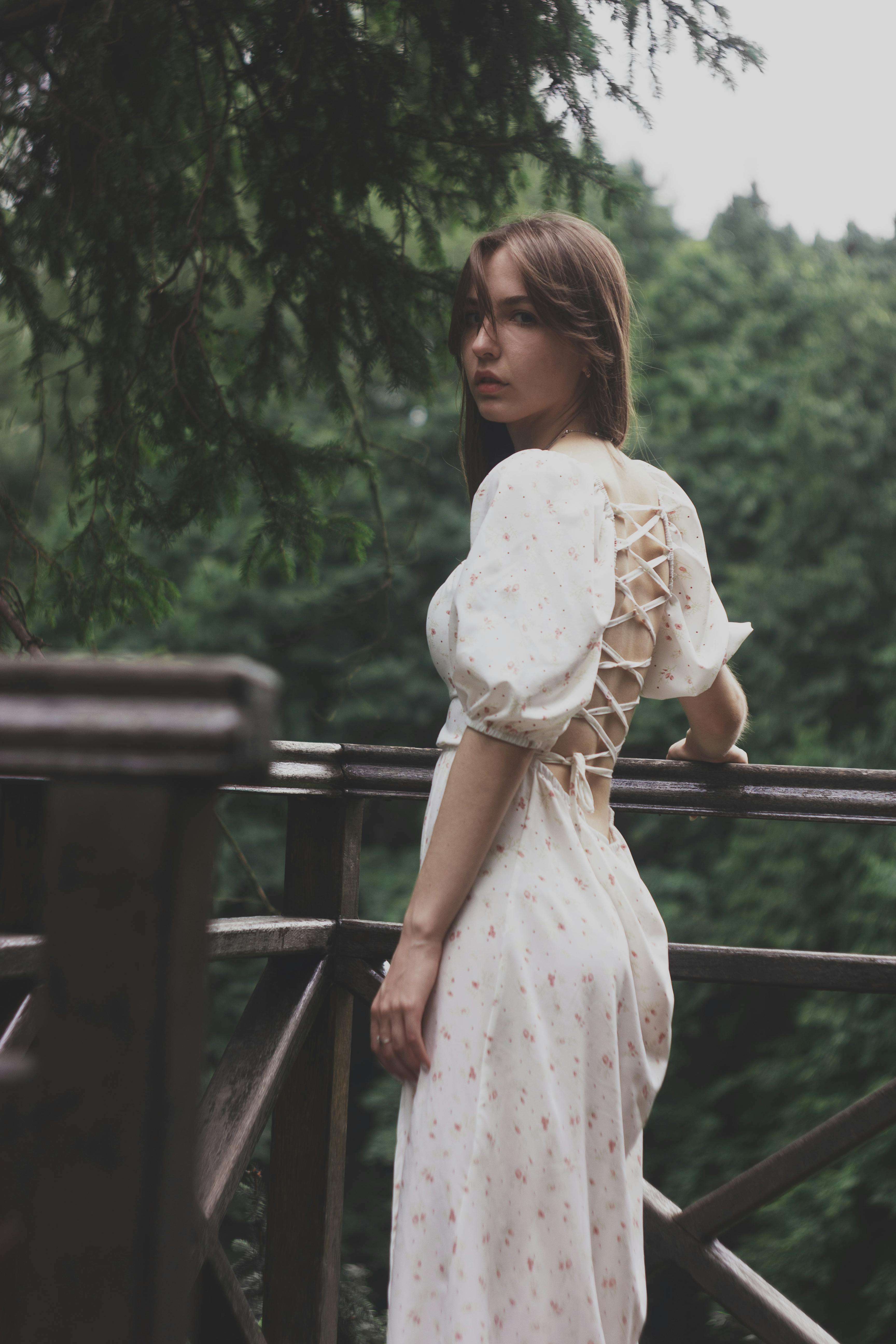 Elegantly dressed woman stands on a railing in a lush Ukrainian forest, capturing serene beauty.