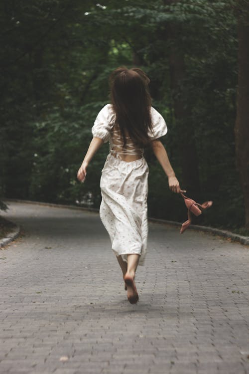 Free A Back View of a Woman in White Dress Running on the Street Barefooted Stock Photo