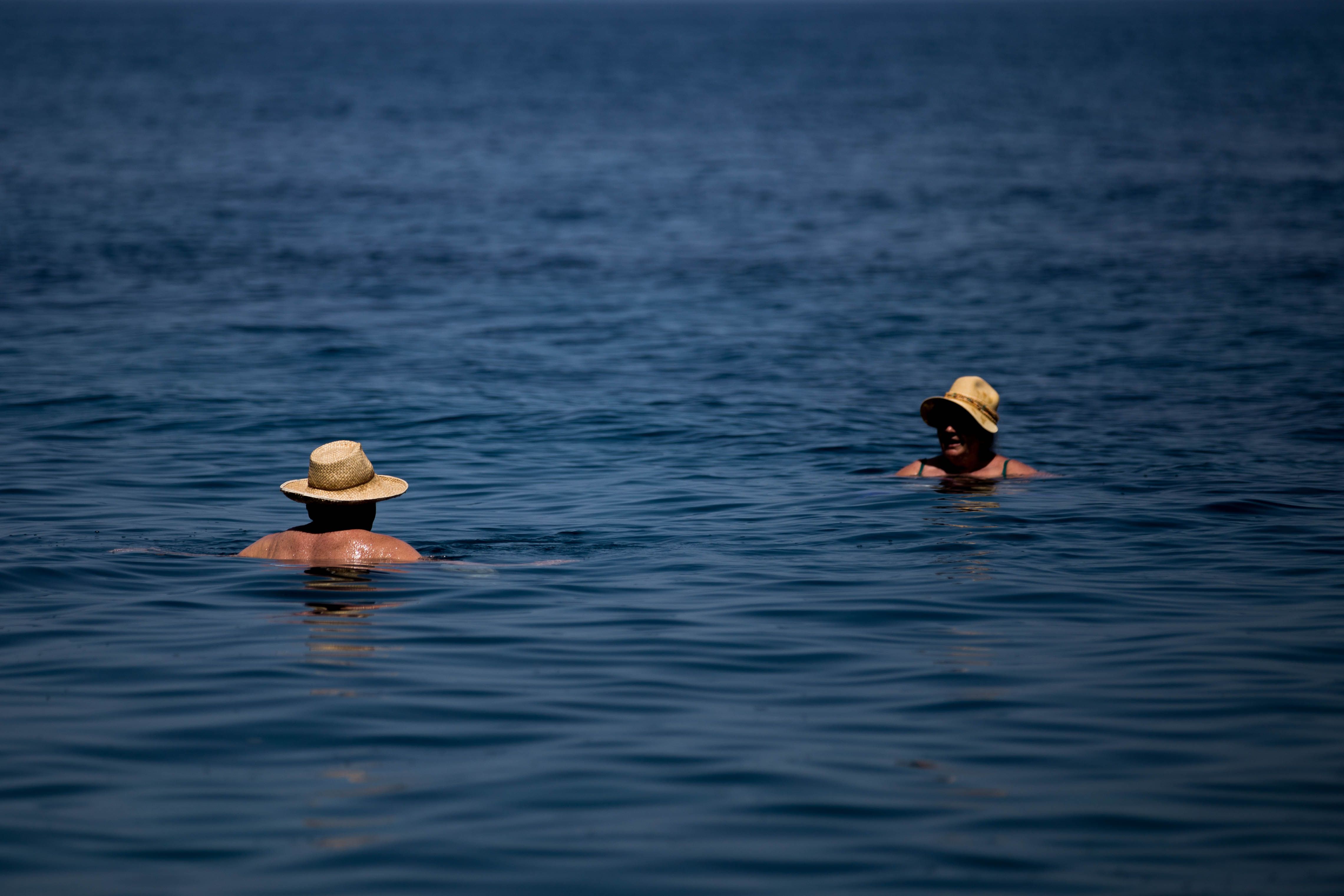 A couple swimming in the clear blue sea, both wearing straw hats on a sunny day.