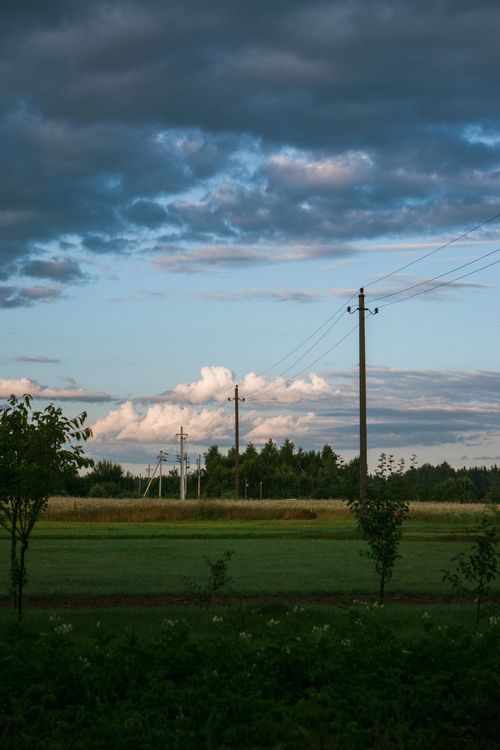 Free Tranquil rural landscape featuring telegraph poles, green fields, and dynamic cloud formations. Stock Photo