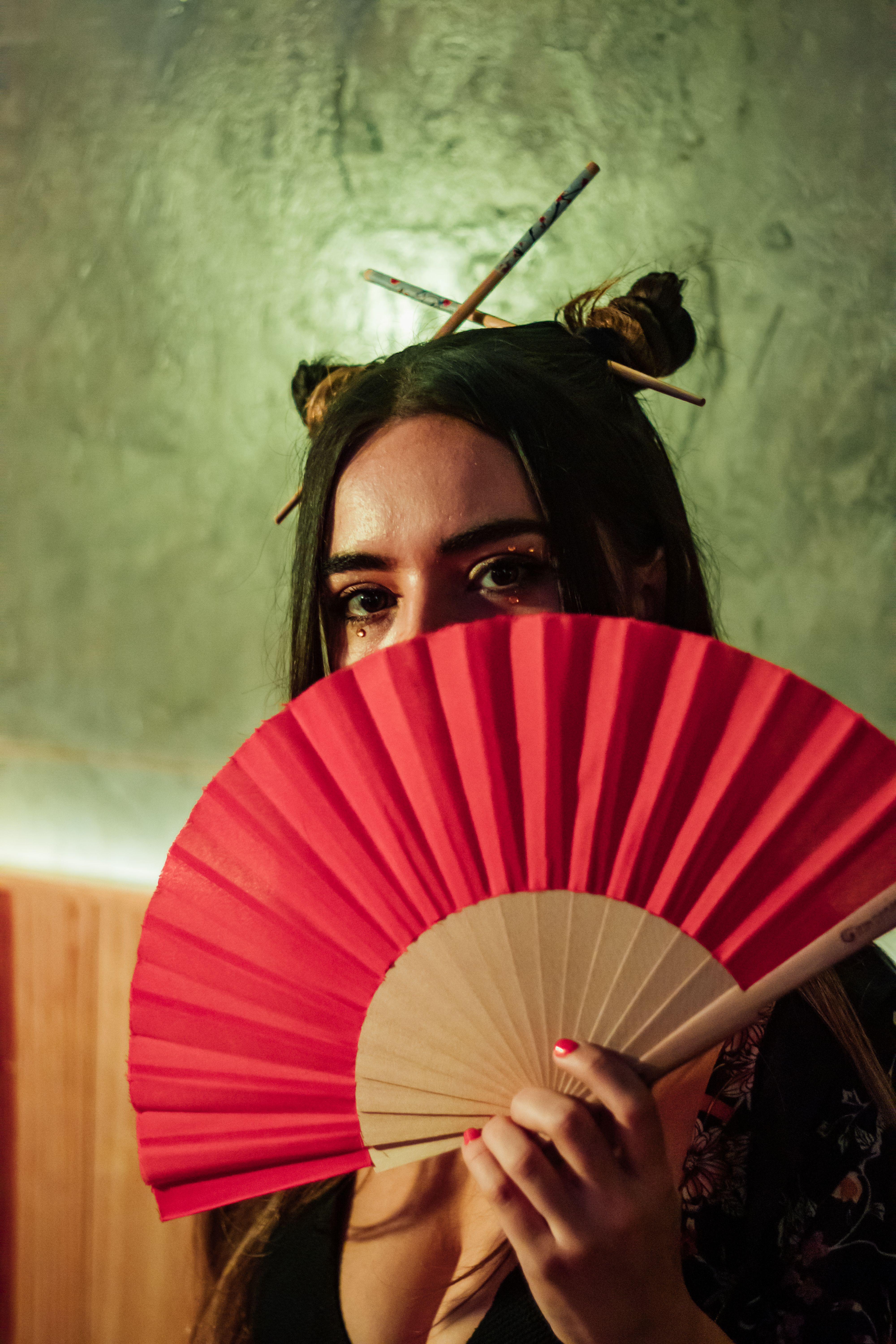Captivating portrait of a woman half-hidden behind a red fan, evoking a sense of mystery and elegance.