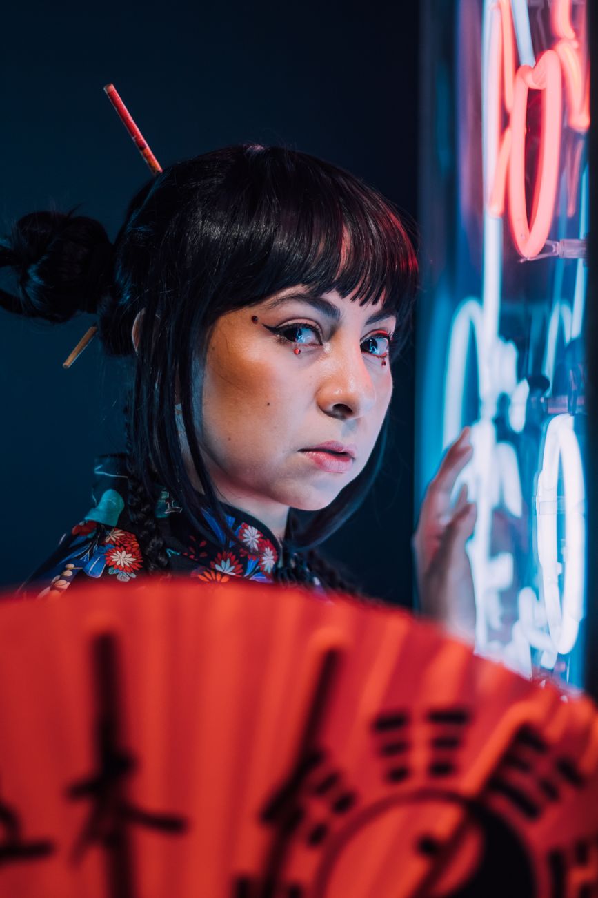 Close-up portrait of a woman with a fan in neon lighting.