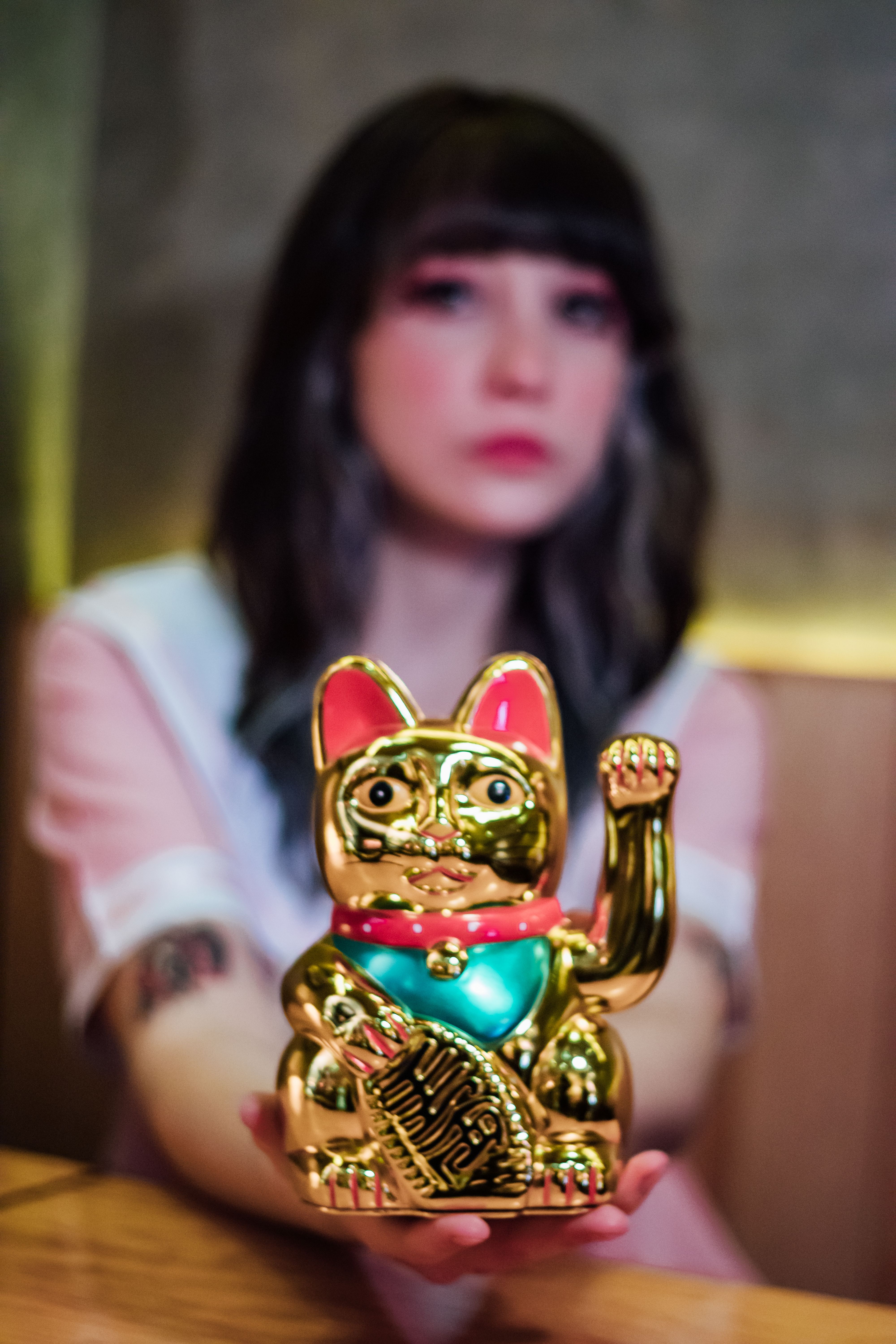 Blurred woman presenting a golden Maneki-neko figurine in a cozy indoor space.