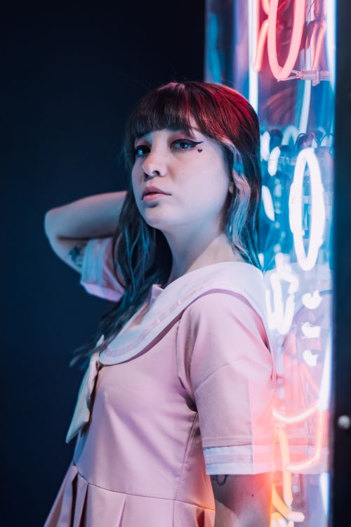 Free Portrait of a fashionable young woman in a pink dress posing by neon lights. Stock Photo