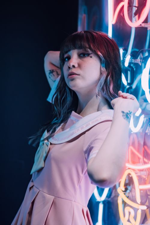 Free Portrait of a young woman with bangs posing against a backdrop of neon lights. Stock Photo