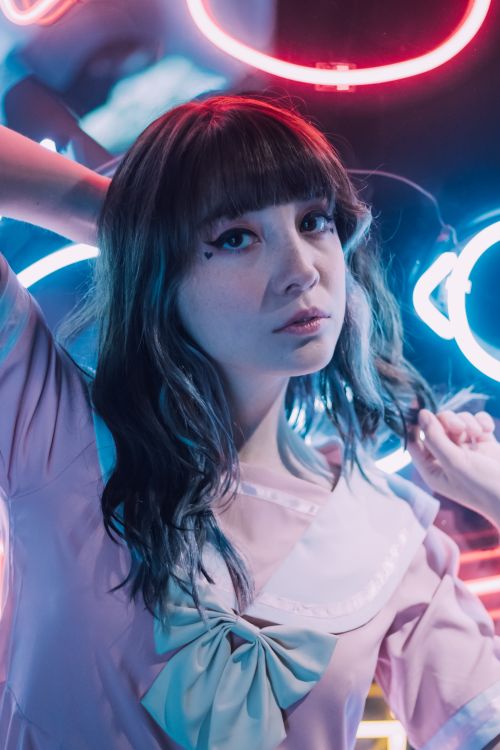 Free Portrait of a young fashionable woman in a pink dress posing confidently amidst vibrant neon lights. Stock Photo