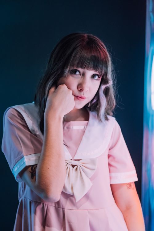 Free Portrait of a woman with bangs in a pastel pink sailor dress posing indoors with soft lighting. Stock Photo