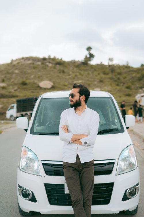 Free Man in sunglasses and white shirt leaning on a car with arms crossed outdoors. Stock Photo