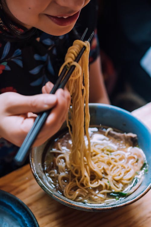 Free Person Eating Japanese Noodles in Blue Ceramic Bowl with Black Chopsticks Stock Photo