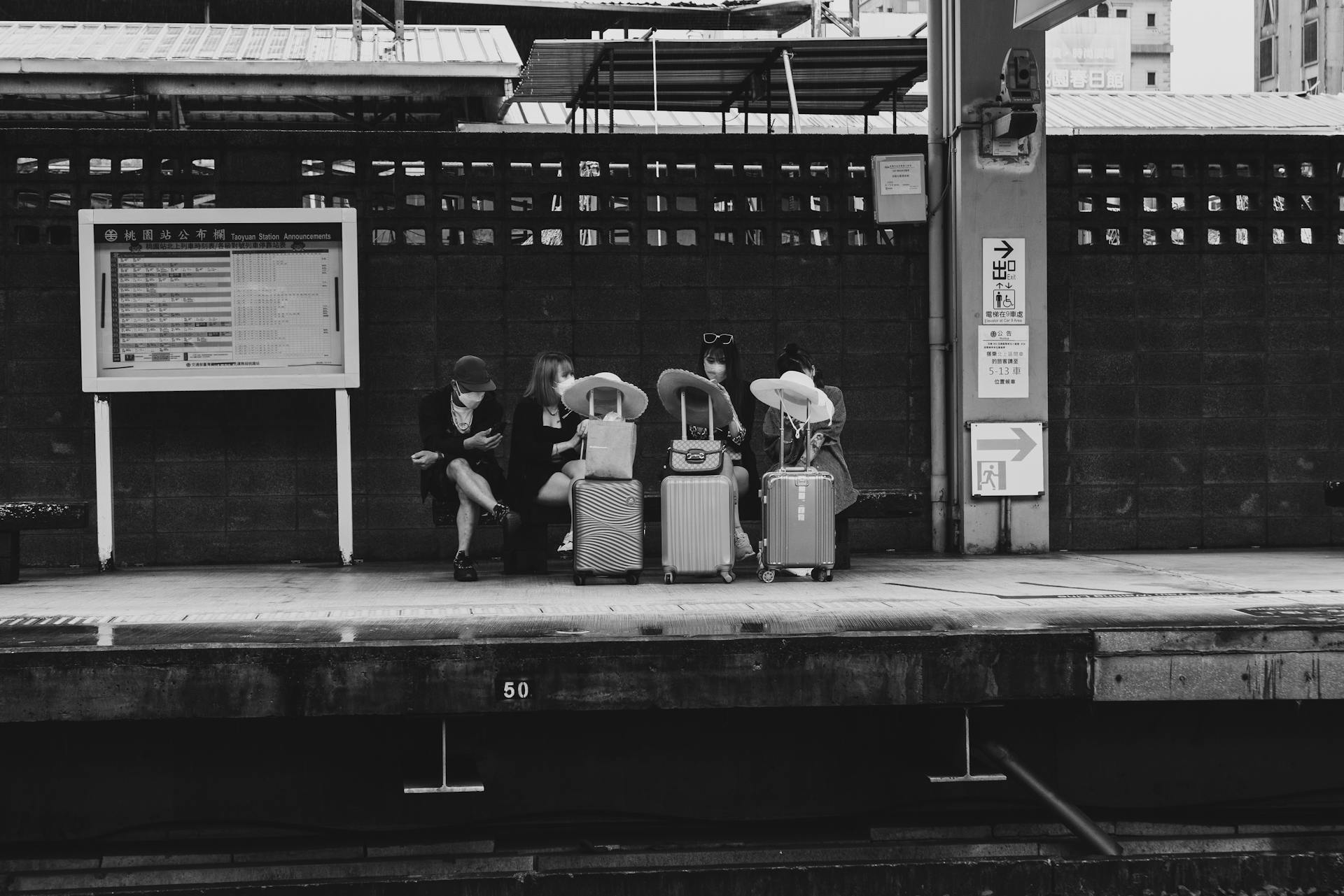 Monochrome image of travelers with luggage at an urban railway platform.