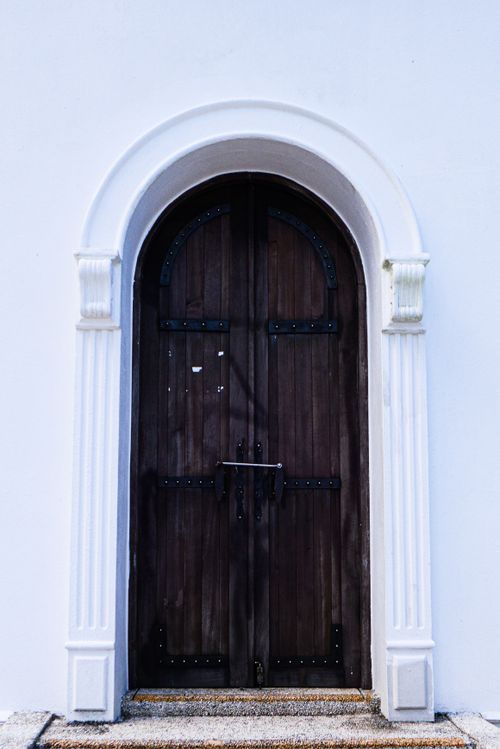 Free A stylish brown wooden door with intricate metalwork set in a pristine white archway. Stock Photo