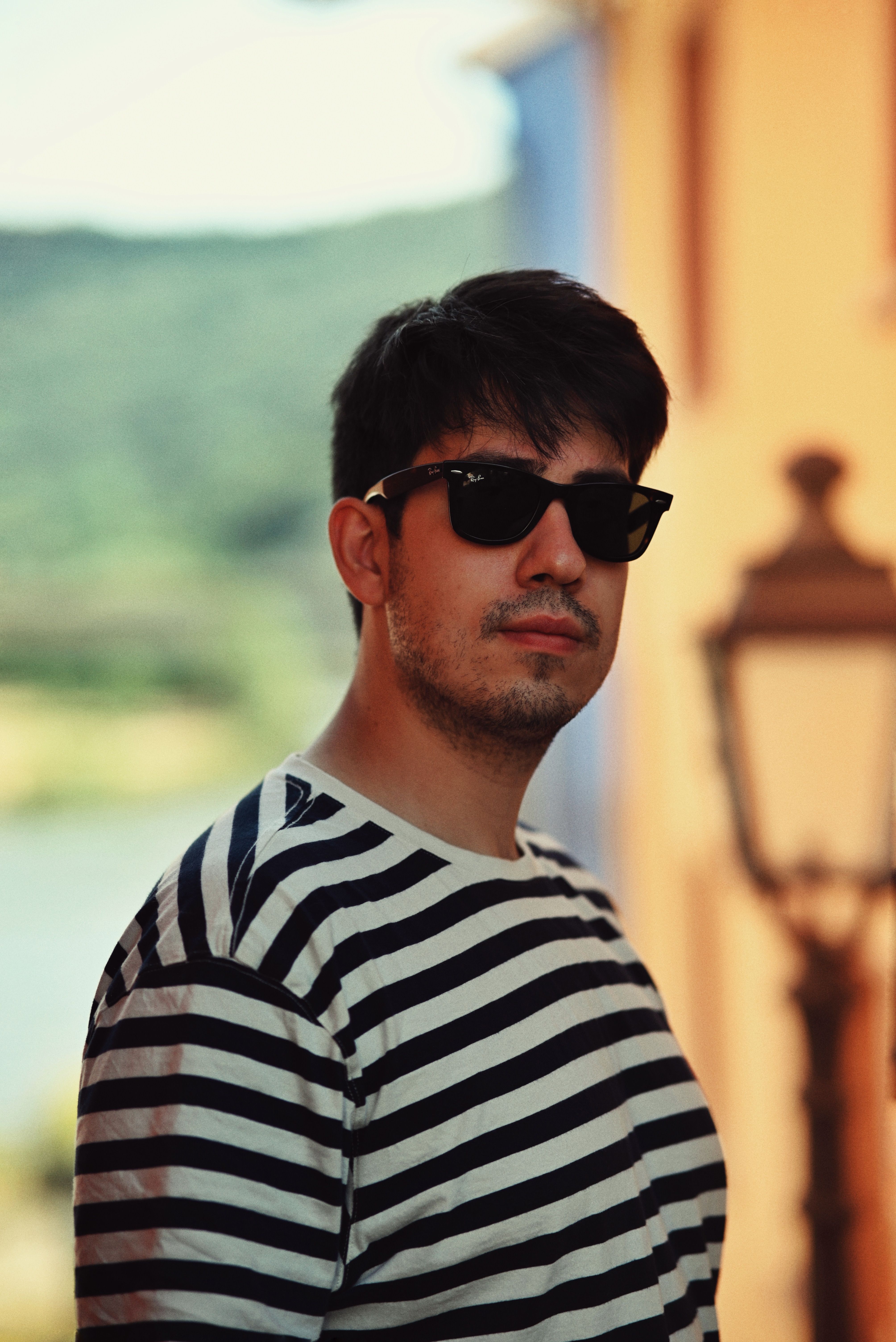 A fashionable man outdoors wearing sunglasses and a striped shirt in vibrant setting.