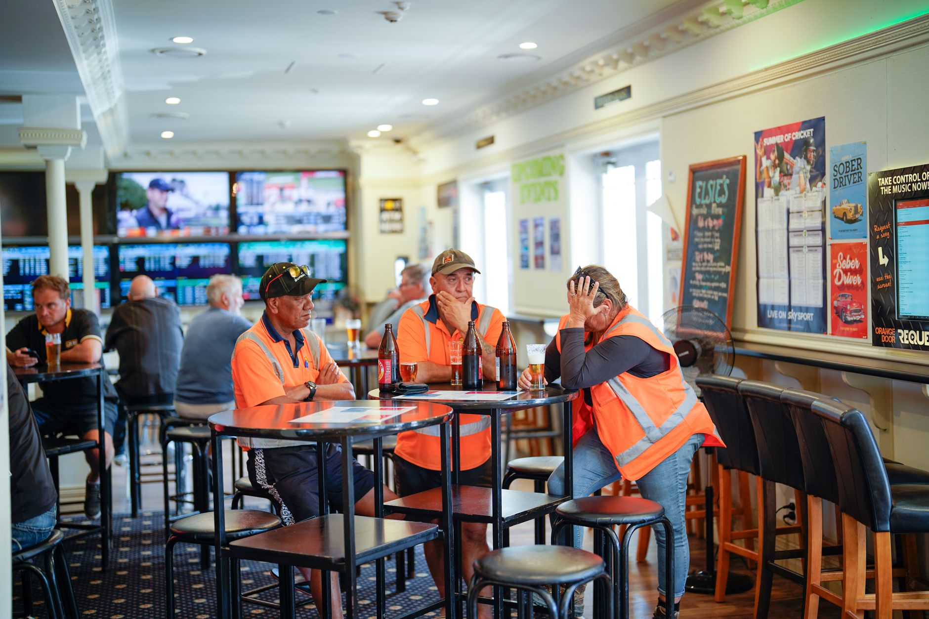 Workers in reflective vests enjoying drinks at a pub in Tuakau, New Zealand.