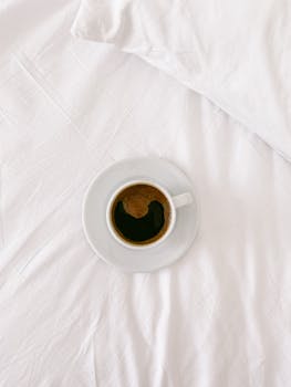 A cup of espresso sits on white sheets, offering a calm and inviting morning vibe.