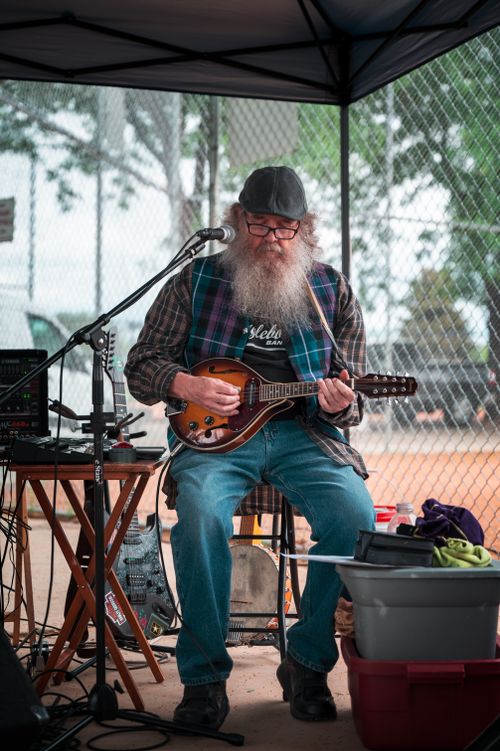 Free Senior man with beard playing mandolin at outdoor music performance under a tent. Stock Photo