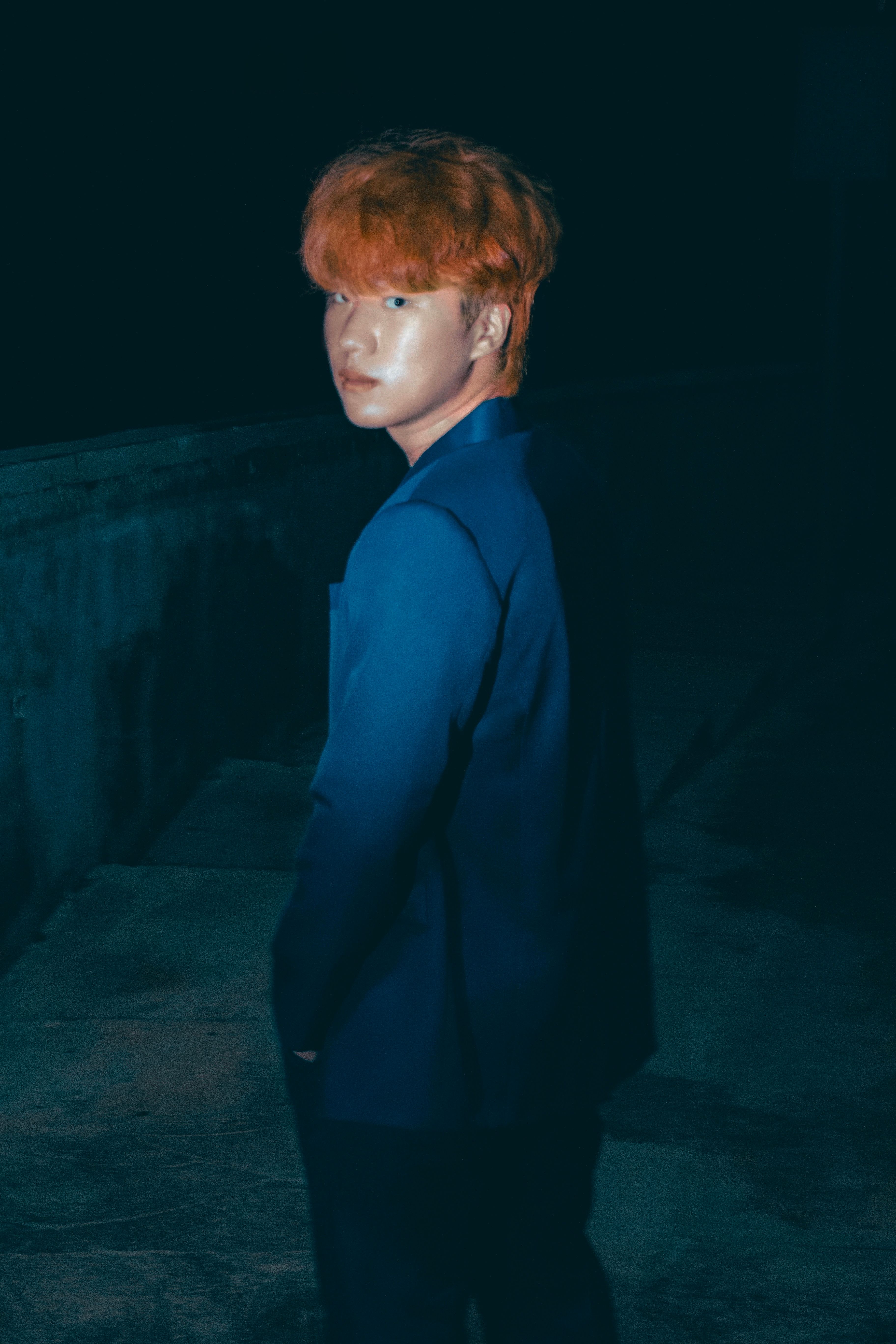 Fashionable young man with ginger hair in a blue suit, illuminated against a night backdrop.