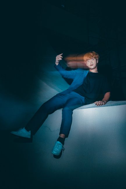 Fashionable Asian man in blue suit with artistic motion blur against dark background, posing confidently.