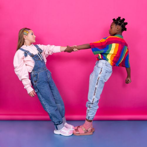 Two children in bright striped and denim outfits on a pink backdrop — photo by Cristiano Silva on Pexels