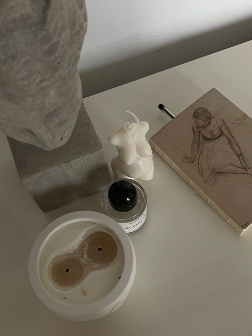 Free Artistic still life featuring a torso candle, sketchbook, and sculpture on a table. Stock Photo