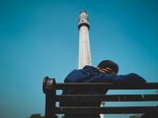 Man sitting on a bench near Shahid Minar, Kolkata under clear blue skies.