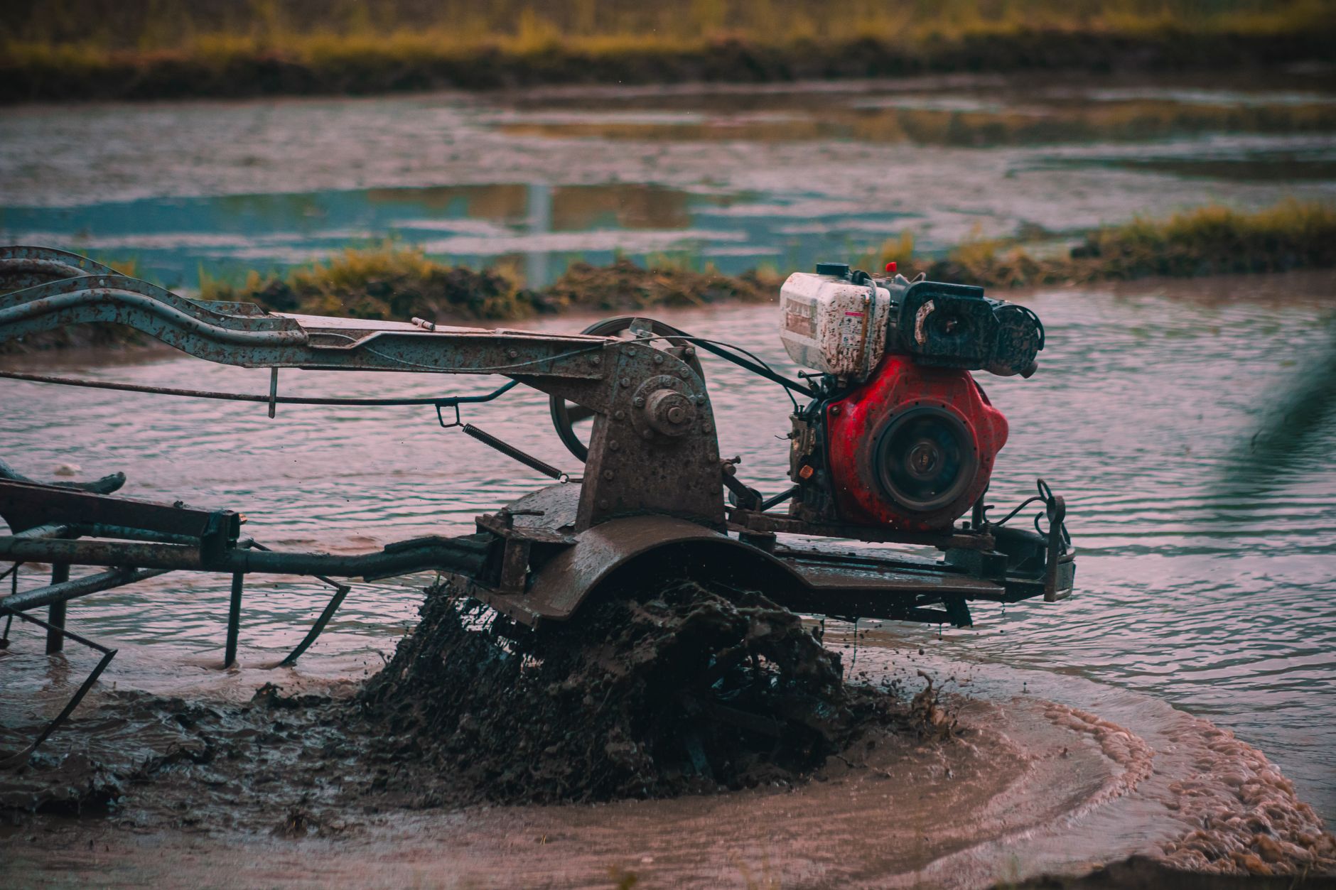 Close-up of a tractor plowing through waterlogged farmland, preparing for cultivation.