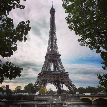 View of the Eiffel Tower framed by trees under a partly cloudy sky in Paris, France.