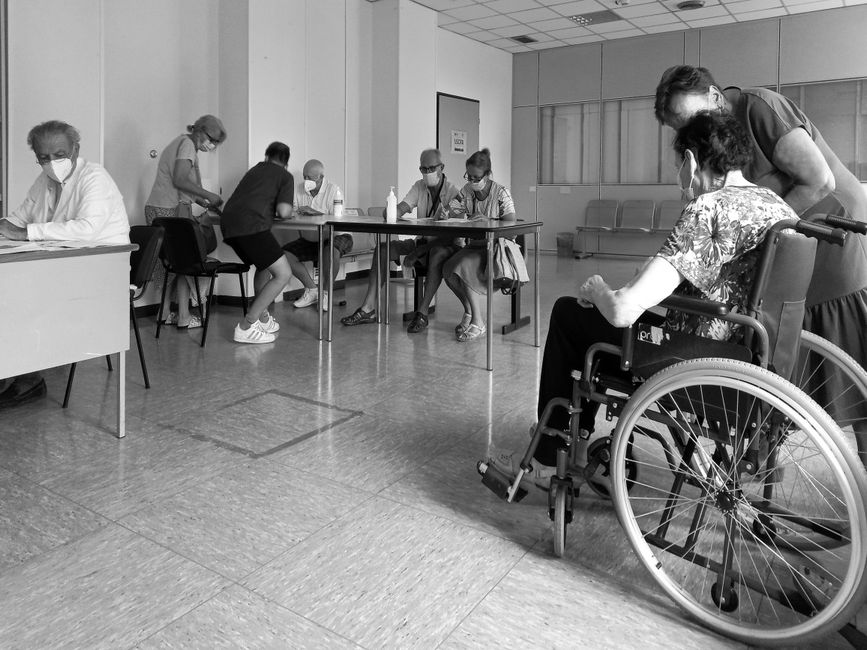 Personas con mascarillas en una sala de espera de hospital, interactuando y manteniendo distancia social.