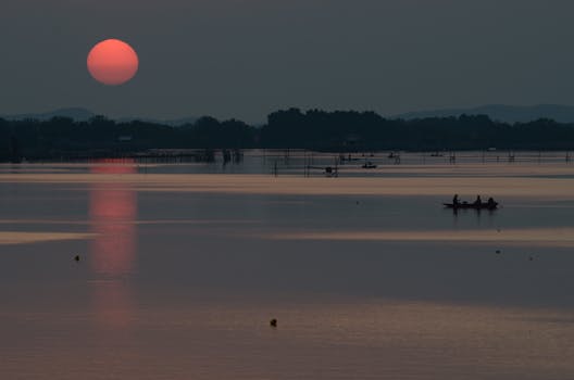 Silhouetted boats on a tranquil river during sunset in Chanthaburi, Thailand, reflecting the golden hues.