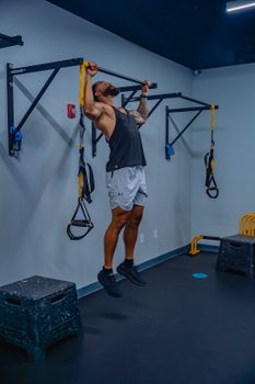 A strong man working out with pull-up bars indoors, showcasing fitness and strength.