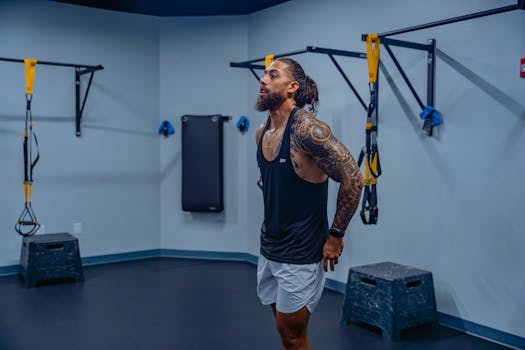 Fit man with tattoos working out in a gym wearing tank top, showcasing muscular physique.