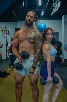 A strong couple lifting dumbbells in a gym, showcasing their fitness and tattoos.