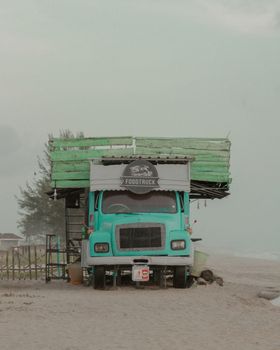 Vintage turquoise food truck parked on a misty beach, creating a serene and nostalgic atmosphere.